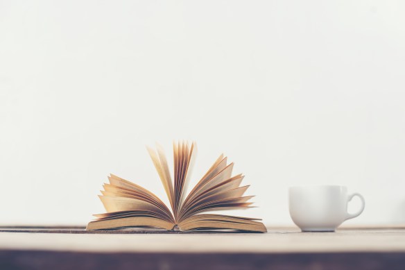 Vintage old book with coffee cup on wooden deck table background